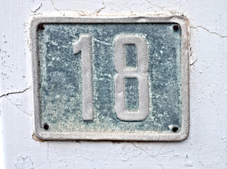 Number 18, eighteen, weathered blue plate on a white wall.