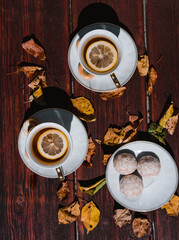 Black tea with lemon and sweets in nature, tea ceremony for two. Beautiful white ceramic tea set on a wooden table, next to the fallen yellow autumn leaves from the trees.