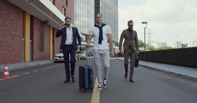 three men walk down the street. A man with a travel bag.