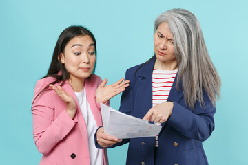 Displeased bewildered asian female business women employer and employee in pink blue jackets posing working in office hold papers documents spreading hands isolated on blue background studio portrait.