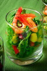 A salad of mango, sweet pepper, rukkola and garlic-fried shrimp in a glass. Close up. Selective focus. Green background.