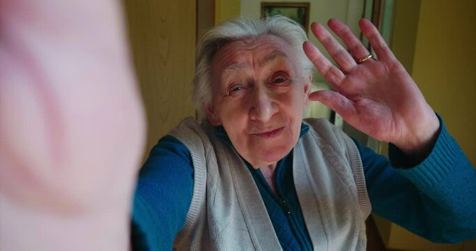 Authentic shot of a happy grandmother is making a selfie or video call to relatives with a smartphone at home. Concept of technology, modern generation,family, connection, authenticity