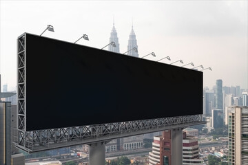 Blank black road billboard with Kuala Lumpur cityscape background at day time. Street advertising poster, mock up, 3D rendering. Side view. The concept of marketing communication.