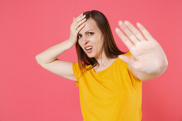Displeased dissatisfied young brunette woman 20s wearing yellow casual t-shirt posing standing put hand on head showing stop gesture wth palm isolated on pink color wall background studio portrait. © ViDi Studio