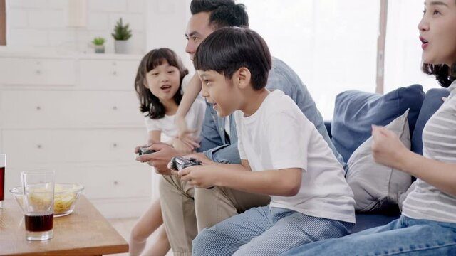 Candid of happy asian family play video game at home feeling excited fun holding console in hand in quarantine activity, entertainment at home concept. Competition and funny in leisure time or hobby.