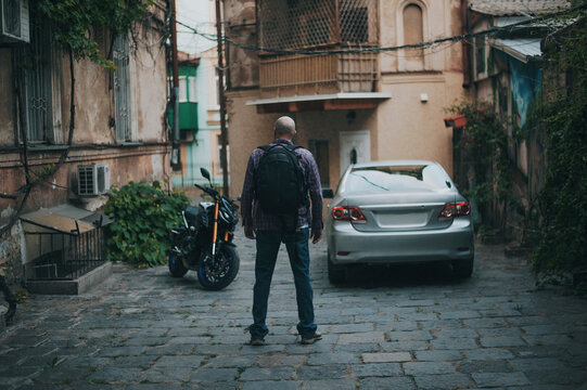 Fototapeta Bold man with backpack watch on moto and car at italian style street. 