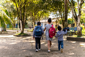 three children walking hand in hand in a park with school bag