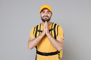 Delivery employee man guy male 20s in yellow cap t-shirt uniform thermal food bag backpack work courier service during quarantine coronavirus covid-19 virus, posing isolated on gray background studio.