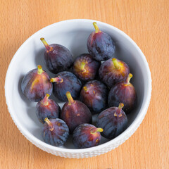 Figs fruits in a bowl on wooden background, top view.