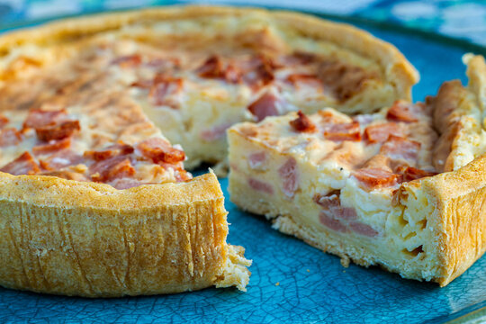 Quiche Lorraine tart on a turquoise plate with a slice cut out.