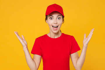 Obraz na płótnie Canvas Delivery employee woman in red cap blank t-shirt uniform workwear work courier in service during quarantine coronavirus covid-19 virus, spreading hands isolated on yellow background studio portrait.