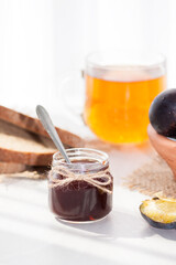 Sweet homemade plum jam and fruits on a white table in a sunny day.