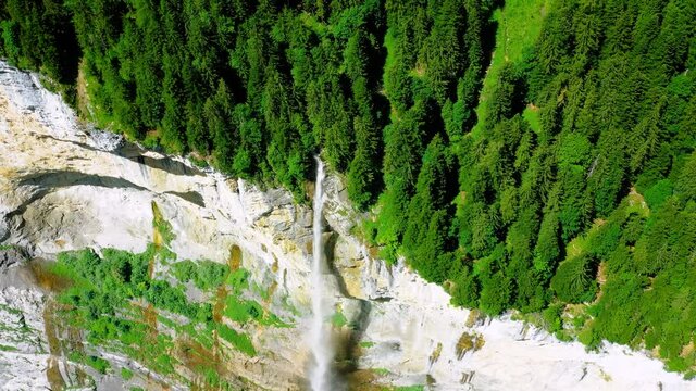Staubbach Falls in Switzerland. A waterfall surrounded by the green forest of the Alps - 4K aerial drone view above the cliff
