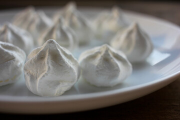 Close-up of meringue on a white plate. Marshmallows on wooden table background