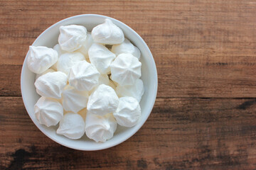 Close-up of meringue in a white bowl. Marshmallows on wooden table background. Flat lay, copy space