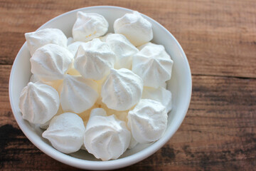Fototapeta na wymiar Close-up of meringue in a white bowl. Marshmallows on wooden table background. Flat lay, copy space