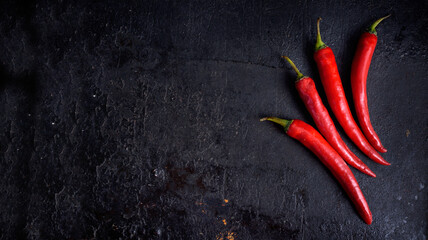 Red hot chili peppers on black rustic textured slate from above. Food background with spicy chilli...