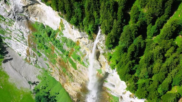 Staubbach Falls in Switzerland. A waterfall surrounded by the green forest of the Alps - 4K aerial drone view above the cliff