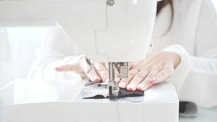Female hands sew on a white sewing machine close-up. Concept of sewing in modern bright studio,...