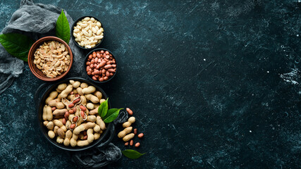 Obraz na płótnie Canvas Set of peanuts in bowls on a black stone background. Nut background. Top view.