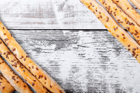 Breadsticks of puff pastry with flax seeds against the white wooden background