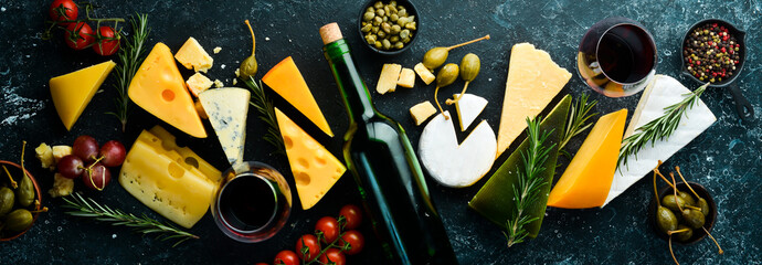 Wine, cheese and snacks on a black stone background. Assorted cheese. Top view. Free space for your...