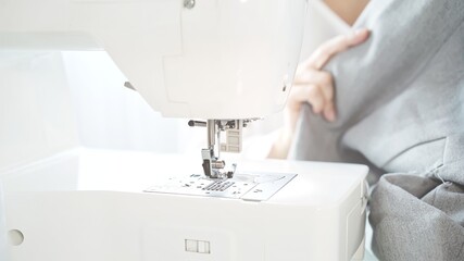 Concept of sewing courses in modern bright studio, sewing in process, blurred background. Female hands sew on a white sewing machine close-up. 