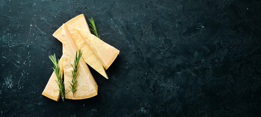 Piece of solid cheese on a black stone background. Parmesan. Top view. Free space for your text.