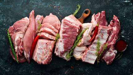 Raw meat background. Meat on a black stone background with spices and herbs. Top view. Rustic style.