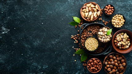 Obraz na płótnie Canvas Assortment of nuts: pistachios, hazelnuts, pine nuts on a black stone background. free space for your text. Top view.