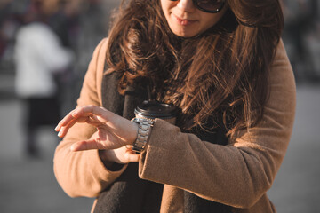 woman outdoors check time on wrist watch holding paper coffee cup