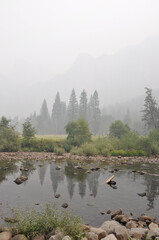 Hazy and smokey view of the Merced River, trees and mountains in Yosemite National Park, during...