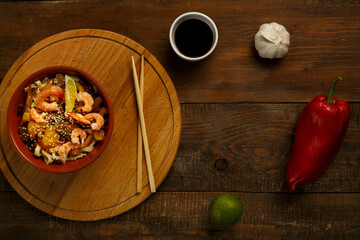 udon with mushrooms and shrimps in a clay plate on a round stand next to chopsticks and ingredients.