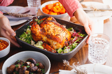 Hands put a dish with whole roasted chicken on a festive table. The concept of family dinner or Thanksgiving celebrate