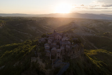 Fototapeta na wymiar Aerial view of stone town Civita di Bagnoregio with the sun at the sunrise with clay badlands and trees in background