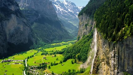 Small village near a waterfall in Switzerland. A valley surrounded by the green forest of the Alps - 4K aerial drone view