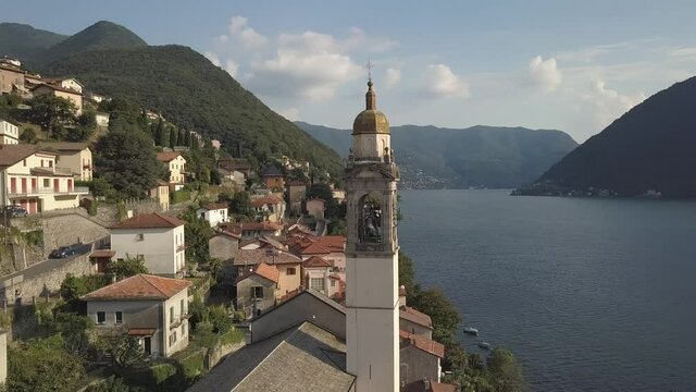 Aerial of a Church Clock Tower in a little Village in Italy by a lake in the summer, Nesso, Como lake, Italia