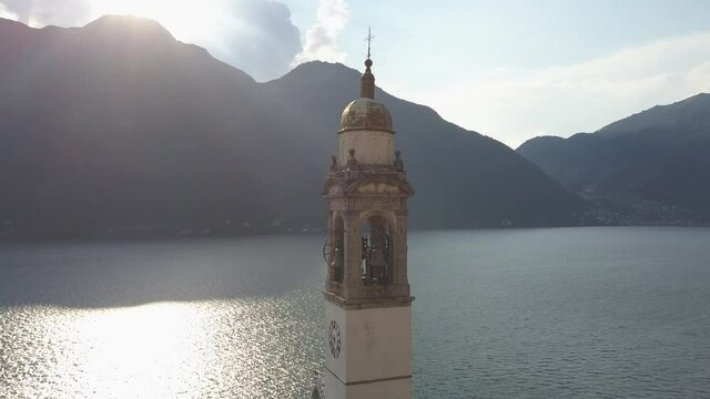 Rotating shot of a church clock tower in a beautiful landscape with lake and mountains, Nesso, Como lake, Italy