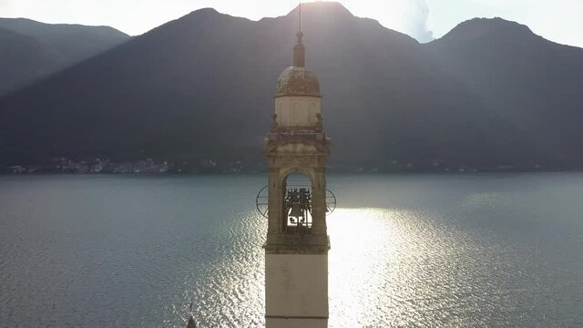 Sliding shot of a church clock tower behind Como lake with mountain range, Nesso, Italia