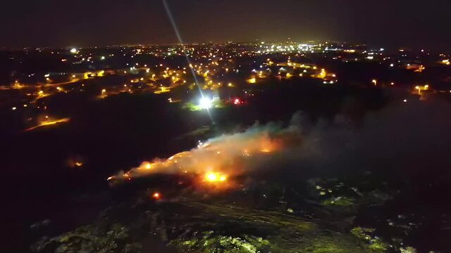 Aerial view around a fire at a junkyard, city in the background, during night time, in Evento, Santo Domingo, Dominican Republic - Orbit, drone shot