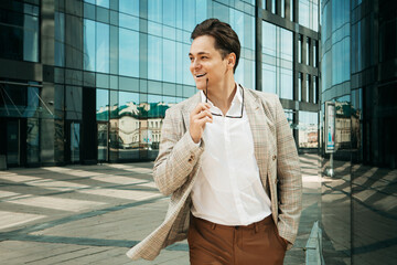 Young happy man in a business suit poses near a modern business center on a summer day