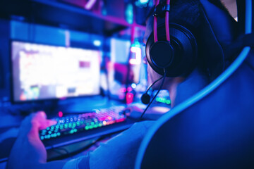 Fototapeta na wymiar Young man gamer play online video games with headphones in internet club cafe, blue color. Esports concept