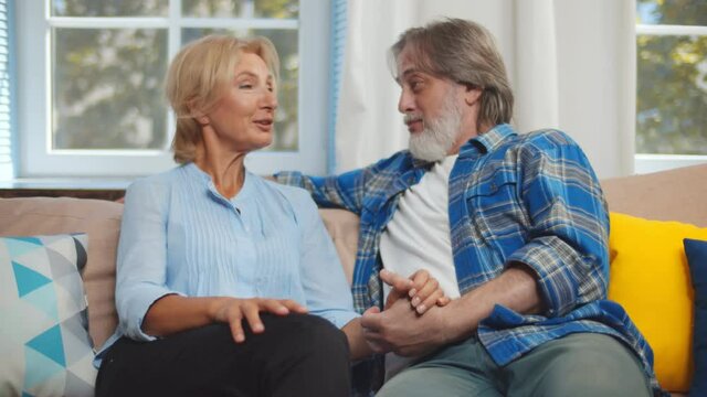 Happy senior couple talking while sitting on couch in cozy home interior