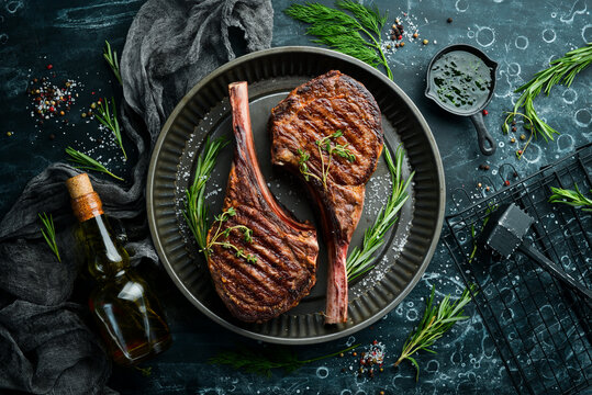Juicy steak grilled on the bone with spices and herbs. On a black stone background. Top view. Free copy space.