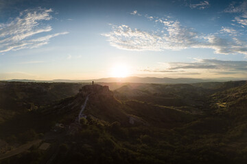 Fototapeta premium Aerial view of stone town Civita di Bagnoregio with the sun at the sunrise with clay badlands and trees in background