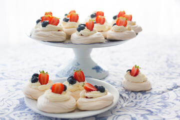 Homemade meringue Pavlova cakes with fresh berries: strawberry and blueberry on white platter on light blue tablecloth