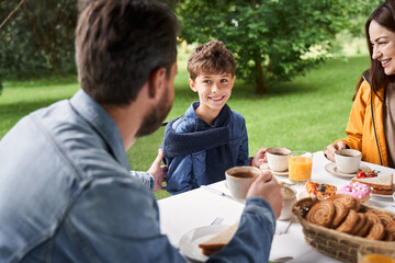 Cheerful boy having breakfast with parents outdoors