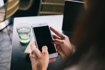Cropped image of female millennial share media and publication in blog using smartphone with empty screen, woman's hand holding mobile phone making booking online and transaction via application
