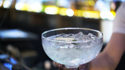 Cocktail glass with cubes of ice , close up, on blurry background of barman at bar. Cocktail glass focused shot and barman inside on blurred background, making cocktail concept
