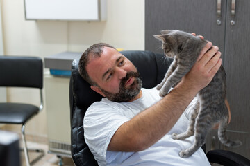 Middle age bearded man playing at his office with beautiful little kitty